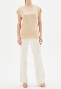 Beige v-hals t-shirt med korta ärmar, i kombination med vita vida byxor. T-shirten har en slät textur och en avslappnad passform.