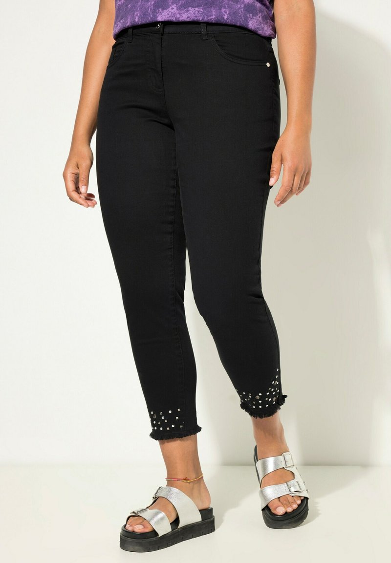 Jeans negros ajustados con dobladillos deshilachados, adornados con tachuelas plateadas en los tobillos. Combinados con sandalias de plataforma plateadas y una blusa morada.