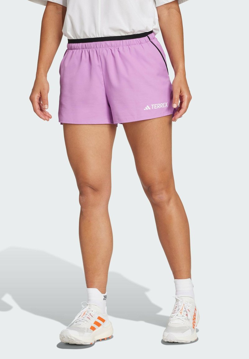 Pantalones cortos deportivos morados con una cinturilla elástica, detalles en negro y el logo "TERREX" en blanco. El material parece ligero y suave.