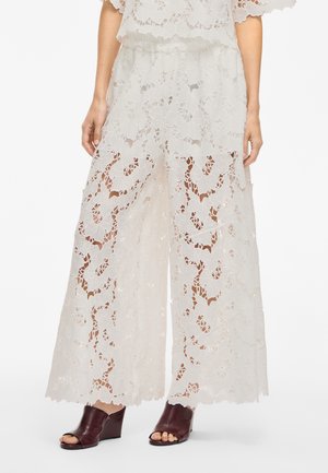 Weiße Spitze weite Hose mit floralem Muster, transparentem Design und elastischem Bund. Kombiniert mit bordeauxfarbenen offenen Absätzen.