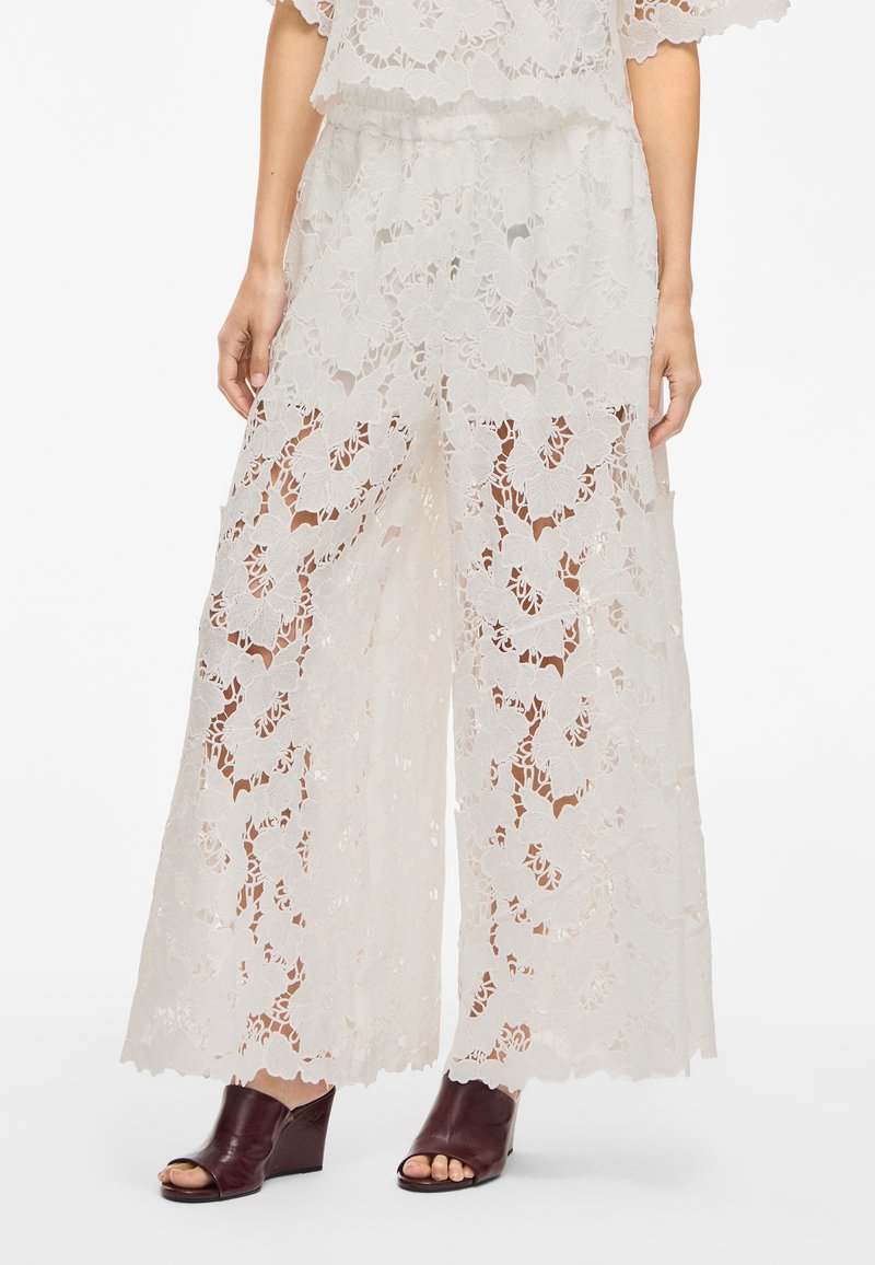 Weiße Spitze weite Hose mit floralem Muster, transparentem Design und elastischem Bund. Kombiniert mit bordeauxfarbenen offenen Absätzen.