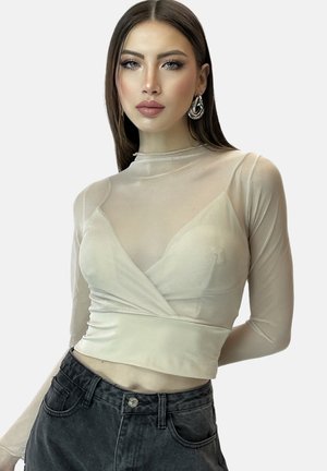 Beige, langärmliges, durchsichtiges Oberteil mit Wickeldesign und hohem Kragen; kombiniert mit hoch taillierten schwarzen Denim-Jeans. Glatte Texturen und taillierte Passform.