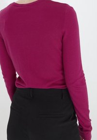 Fuksjowy sweter z długim rękawem wykonany z miękkiego dzianinowego materiału, z okrągłym dekoltem i dopasowanym krojem, zestawiony z czarnymi dopasowanymi spodniami.