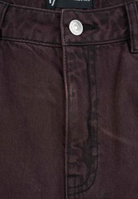 Zbliżenie na granatowy pas dżinsów z metalowym guzikiem i widocznymi detalami szwów.