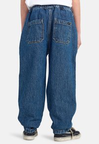 Lichtblauwe denim baggy jeans met een hoge elastische tailleband, twee achterzakken en een rechte pasvorm. Gecombineerd met zwart-witte schoenen.