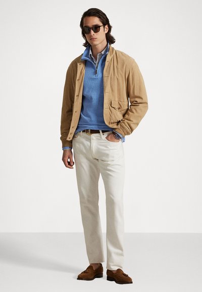 Casaco bege de botão, suéter azul, calças brancas, mocassins castanhos e óculos de sol. Camisa riscada por baixo, design casual com bolsos.