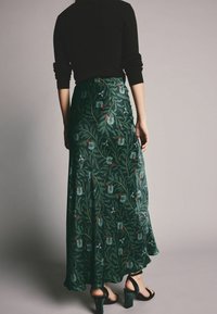 Jupe longue verte avec un motif floral dans des tons rouges et bleus. Fabriquée en tissu fluide, avec une taille ajustée et une légère évasement.