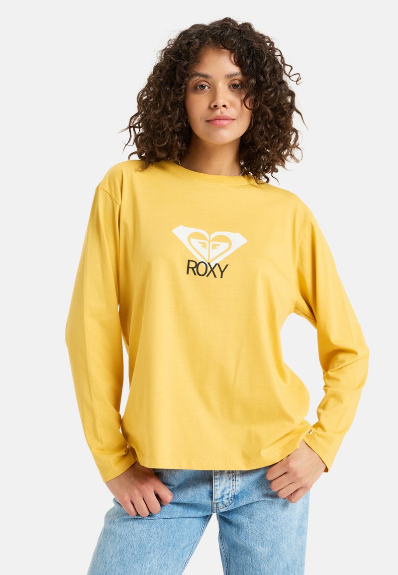 Żółta koszulka z długim rękawem, wykonana z miękkiej bawełny, z białym logo serca i napisem "ROXY" na klatce piersiowej; luźny krój i ściągacze przy rękawach.