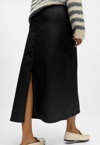 Svart maxikjol med en sidoklyfta. Tillverkad av ett mjukt material, med en rak form och en sydd fåll. Matcher med ljusa loafers.