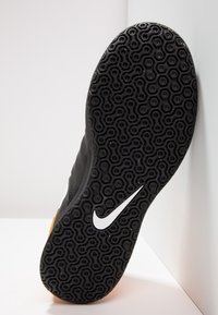 Suela de zapatilla deportiva negra con un patrón de relieve hexagonal y un logo de swoosh de Nike en blanco. Forma ligeramente curvada con texturas elevadas.