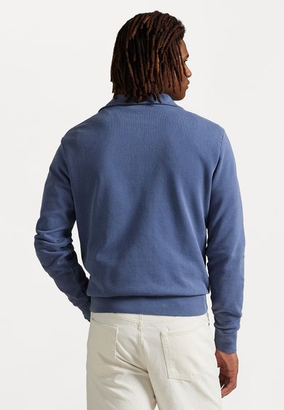 Sudadera de algodón azul con cuello redondo, mangas largas y puños acanalados. Textura suave con un corte holgado y sin patrones visibles.