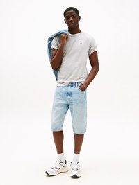 Graues Kurzarm-T-Shirt, hellblaue Jeansshorts und weiße Sneakers mit schwarzen Akzenten. Das Model hält eine Jeansjacke über die Schulter.