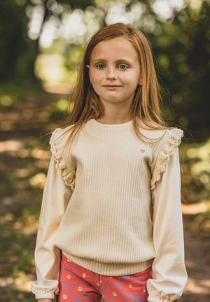 Beige geribbelde trui met ruches, gecombineerd met roze bloemenbroek. Lange mouwen met een losse pasvorm zorgen voor een gelaagde look.