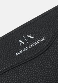 Svart teksturert lommebok med preget logo "A|X ARMANI EXCHANGE" i hvitt. Glatt søm fremhever designet.
