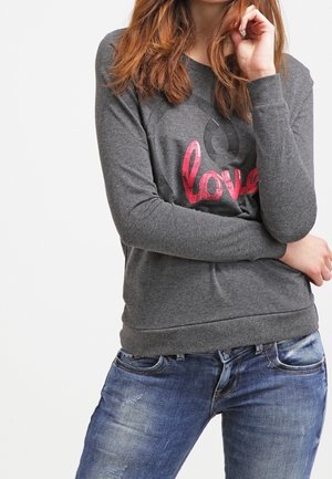 Sudadera gris de mangas largas con un gráfico en rosa que dice "amor", puños y dobladillo acanalados. Combinada con jeans azules desgastados. Textura de tela suave.