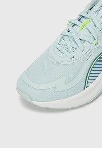 Világoskék sportcipő, texturált anyaggal, sima kiegészítőkkel, hálós részekkel, zöld kiemelésekkel és csíkozott mintával az oldalán.