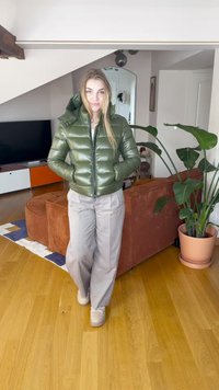 Olivengrøn pufferjakke med lynlås foran, med hætte og en skinnende tekstur. Kombineret med beige bukser med vide ben og sneakers.