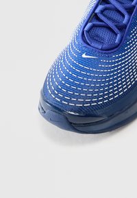 Nike atletske tenisice u plavoj boji s mrežastim gornjim dijelom koji ima bijele zakrivljene šavove, zaobljenim vrhom i ojačanim petom.
