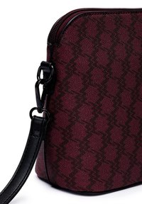 Burgunderfarbene Crossbody-Tasche aus Stoff mit einem strukturierten Zickzackmuster, schwarzen Akzenten und einem abnehmbaren Schultergurt mit einem Schnappverschluss.