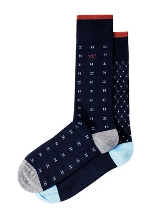 Zwei marineblaue knielange Socken, eine mit hellblauen „H“-Muster und grauer Spitze, die andere mit weißem Diamantmuster und hellblauer Spitze, beide mit roten Bündchen.