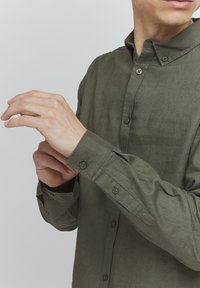 Olive green button-up shirt made of textured fabric, featuring a classic collar, buttoned cuffs, and a slim fit design.