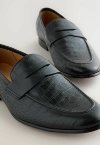 Schwarze Lederloafer mit Krokodilmuster, ausgestattet mit einem strukturierten Riemen an der Vorderseite, runder Zehenform und flachem Absatz.
