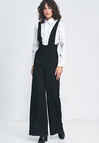 Czarne ogrodniczki o szerokich nogawkach zestawione z białą koszulą zapinaną na guziki. Wykonane z gładkiego materiału, wyposażone w ramiączka i dopasowany krój.