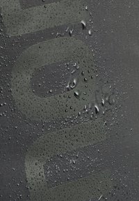 Black textured fabric with water droplets on the surface, featuring large, embossed lettering in a subtle matte finish.