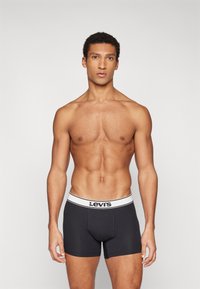 Μαύρα βαμβακερά μποξερές με λευκή ετικέτα Levi's στη μέση, με κομψή εφαρμογή και απαλό υλικό, φορώντας από έναν άντρα μοντέλο.