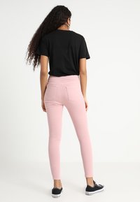 Camiseta de algodón negra combinada con jeans de mezclilla ajustados de color rosa claro y zapatillas negras. Los jeans cuentan con dos bolsillos traseros y detalles en el dobladillo.