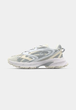 Zapatilla deportiva blanca y gris claro con paneles de malla, suela texturizada y tira para tirar en el talón, vista lateral.
