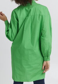 Green oversized shirt dress in lightweight fabric, featuring long sleeves, a buttoned cuff, and a straight cut with a back yoke detail.