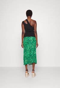 Musta olkapäättömyystoppi yhdistettynä vihreä-siniseen marmorikuvioituun midihameeseen, jossa on ilmava ja rento istuvuus. Vaaleat korolliset sandaalit.