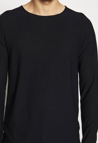 Svart långärmad t-shirt i mjukt tyg med rund halsringning och slim fit, med minimala sömdetaljer.