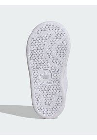 White sneaker sole featuring a textured pattern with hexagonal grooves and a prominent Adidas logo at the heel. Smooth rubber material.