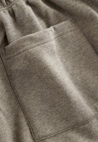 Szary bawełniany materiał o teksturowanym wykończeniu, z podwójnie szytą kieszenią z przodu, tworzący swobodny i funkcjonalny design.