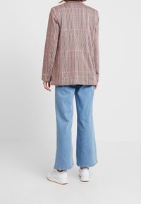 Rutig, långärmad kavaj i rosa och beige nyanser, matchad med ljusblå vida jeans och vita sneakers. Strukturerad tyg, skräddarsydd passform.