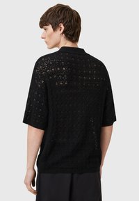 Polo de punto negro de manga corta, con un patrón de encaje, tejido texturizado, tejido abierto y cuello. La vista trasera muestra un ajuste relajado.