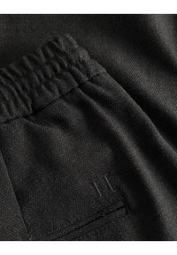 Tissu noir avec un subtil motif en chevrons, doté d'une taille élastique et d'un petit détail brodé, montrant texture et douceur.