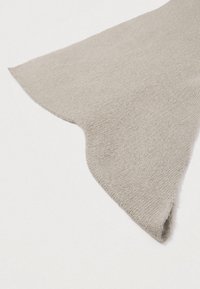 Jemná béžová pletenina s vlnitým okrajem na bílém pozadí, zdůrazňující texturu a detaily.