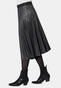 Grijze geplooide rok met een glanzende textuur, zwarte elastische tailleband, gestyled met zwarte enkellaarzen met een puntige neus en blokhak.