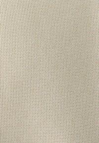 Tissu beige texturé avec un motif tricoté, présentant de petites boucles tout au long, créant une apparence dense et chaleureuse.