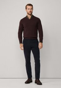 Tamno burgundska V-izrez pulover preko zelene košulje s ovratnikom, u kombinaciji s mornarskim slim-fit hlačama i smeškim čipkastim čizmama. Jednostavan dizajn i tekstura.