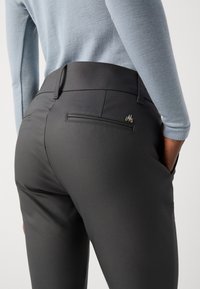 Pantalon noir à la texture lisse, avec une poche arrière affichant un discret logo et une taille cintrée, porté avec un haut bleu clair.