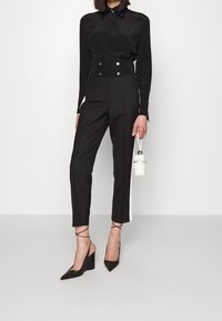 Černá krátká halenka s detaily na knoflíky, v kombinaci s černými kalhotami na míru s bílým bočním pruhem a černými lodičkami s špičatou špičkou. Doplňkem je bílá kabelka.