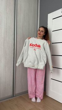 Γκρι φούτερ με κόκκινο λογότυπο "Kodak", διαθέτοντας ριχτό λαιμό και μανίκια με ραφή. Συνδυάζεται με ροζ ριγέ παντελόνια πιτζάμας.