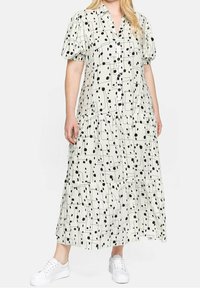 Schwarz-weißer gemusterter Maxikleid mit kurzen Puffärmeln, Knopfleiste, gestuften Design und unterhalb des Knöchels hängend, kombiniert mit weißen Sneakers.