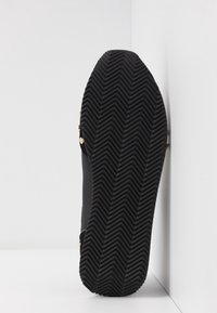 Svart gummisul med ett zigzag-mönster. Har gyllene detaljer nära övre kanten och en slät kantprofil.