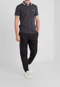 Mörkgrå pikétröja med krage som har turkosa och vita ränder, tillsammans med svarta cargobyxor och vita sneakers.