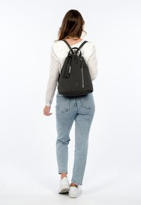 Black, textured drawstring backpack with two shoulder straps, front zipper pocket, and tassel detail. Smooth matte finish, minimalist design.